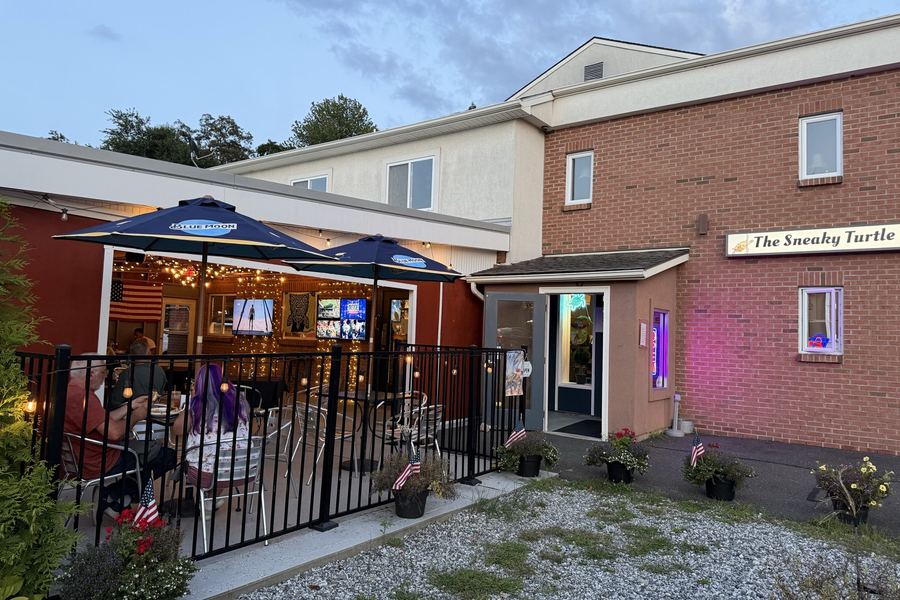 The Sneaky Turtle at dusk, guests at the lit patio tables beside the front door.