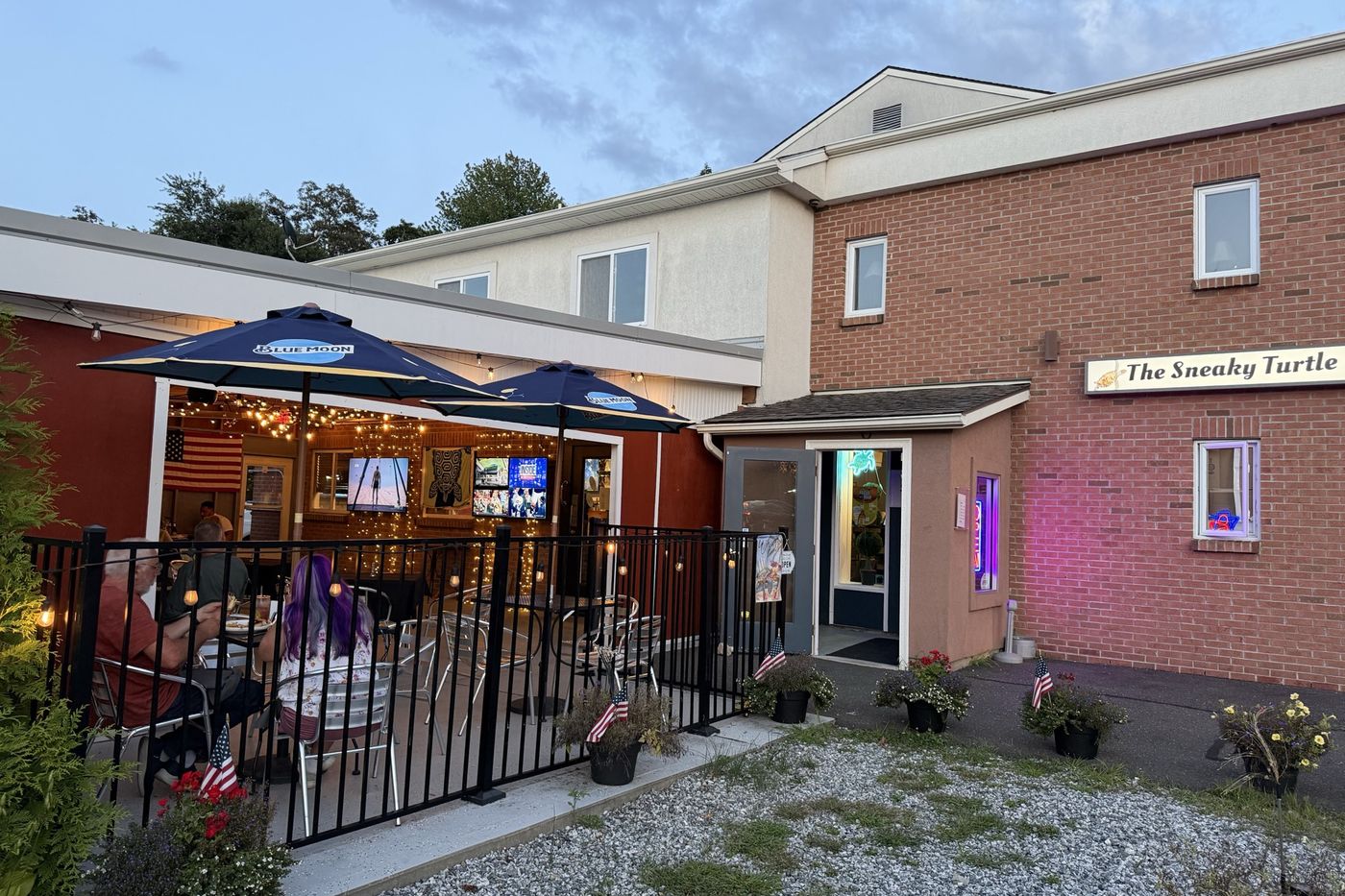 The Sneaky Turtle at dusk, patio umbrellas and string lights lit under the sign.
